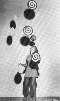 Trixie bounces a ball on her head while doing six plates.