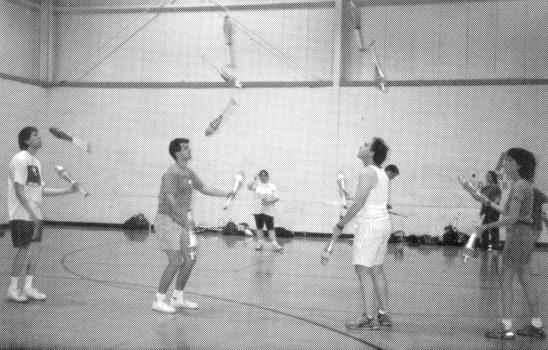 Action at the Up for Grabs Jugglefest.  (l-r) Jim Ellison, Kevin Manes, Todd Claxton and Kathy Glynn od intersecting seven club passing for a total of 13 clubs.  Jim and Todd are passing seven clubs over the head and shoulders of Kevin, while Kevin and Kathy pass sevenover the head and shoulders of Todd.  (Chuck Spreitzer photo)